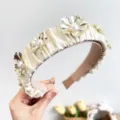 Macro detail of pleated cream headband featuring metallic gold flowers and pearls - Beige