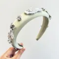 Gros plan d'un serre-tête en satin vert sauge avec des détails de pétales de fleurs en argent. - Fleurs métalliques / Vert clair