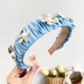 Close-up macro detail of an elegant light blue pleated headband with gold flowers and pearls - Blue