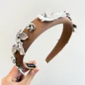 Détail d'un serre-tête rembourré marron avec des fleurs métalliques argentées décoratives - Pétale en Métal Étoile / Marron