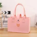 Detailed view of the pink felt tote bag with a cute bear embroidery on a wooden table. - L / Pink