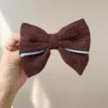Detailed close-up of a burgundy tweed bow hair accessory with light blue piping detail. - Hair Bow