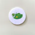 Close-up detail of a white circular badge with a green cartoon shamrock hat design - Clover