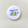 Detail view of a round white felt brooch with a colorful cartoon helicopter design - Helicopter
