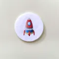 Detailed macro view of a cartoon rocket illustration on a circular white pin badge - Rocket