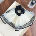 Nahaufnahme von elegantem Mesh-Haargummi mit Falten in Schwarz-Weiß - Cremeweiß mit schwarzer Paspel (Rock-Stil)