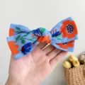 Gros plan d'une pince à cheveux bohème brodée en forme de nœud bleu tenue dans une main. - Grande Pince Nœud Fleurie Brodée / Bleu