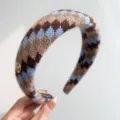 Gros plan d'un serre-tête tricoté Fair Isle rétro avec motifs bleu-brun et logo doré. - Serre-tête Rembourré / Patchwork Bleu Café