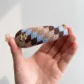 Gros plan d'une pince à cheveux rétro en tricot argyle avec logo M doré. - Barrette Goutte d'Eau / Patchwork Bleu Café