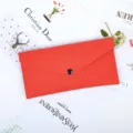 Premium red felt envelope pouch with a minimalist black button closure on a floral flat lay - Orange Red