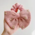 Detailopname van een roze gebreide strik-scrunchie met gouden sterren en woltextuur - Vijfpuntige Ster Stijl / Roze