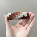 Detail van een retro gebreide haarklem in Fair Isle-stijl met goudlogo - Haarclip / Oranje Koffie Gemengd