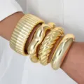 Vista detallada de varios brazaletes de puño dorados pulidos apilados en una muñeca - Estilo de Metal Dorado de 4 Piezas (6686201HB)