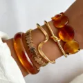 Dettaglio di bracciali rigidi dorati e in resina ambrata sovrapposti sul polso di una donna. - Collezione Bracciali Impilabili Europea (6647501HB) / Ambra Oro