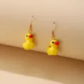 Detailed macro view of cute yellow duck drop earrings with gold fish hooks on beige surface - Little Yellow Duck Style / Lemon Yellow
