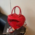 Red heart-shaped handbag with bow detail and adjustable crossbody strap. - Burgundy
