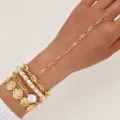 Detalle de una cadena de mano dorada con perlas y conchas en la mano de la modelo - Juego de Concha y Perla Dorada (6695101HB)