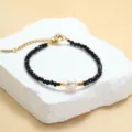 Detaillierte Nahaufnahme des schwarzen Kristallperlenarmbands mit Perle und Goldkettendetails. - Schwarz