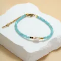 Close-up van blauwe kristalen kralenarmband met zoetwaterparel en gouden kettingdetails. - Inktblauw