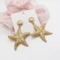 Detailed macro view of gold starfish and shell dangle earrings on a white display card - Shell With Starfish Pendant (1)