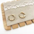 Detailed macro view of gold-tone wavy geometric hoop earrings on a soft grey display pad - Geometric Wave Texture (6) / Gold