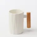 Vue détaillée de la tasse en céramique blanche avec corps facetté et poignée en bois naturel. - Mug blanc à motif losanges