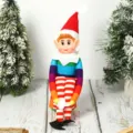Detailed view of a colorful Christmas long-legged elf plush doll toy sitting on a rustic wooden table. - Rainbow Elf