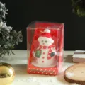 Close-up of Christmas snowman candle in clear packaging box with festive holiday background. - Snowman Candle