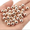 Primer plano de cuentas espaciadoras CCB de oro rosa en la palma para joyería DIY artesanal - 10mm/500g/880 Piezas / Cobre