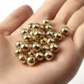 Vista macro de cuentas de CCB de oro metálico brillante en la palma para joyería DIY - 10mm/500g/880 Piezas / Oro claro