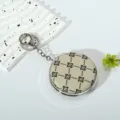 Detail view of a portable round makeup mirror keychain with black floral pattern. - Style 3 (Beige Black Clover)