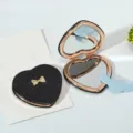 Heart-shaped folding makeup mirror with black glitter finish and elegant gold bow detail. - Heart Shape with Golden Inner Frame (Includes Cloud Comb) / Black (Glitter)