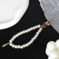 Close-up of elegant white pearl phone strap with a shiny gold-plated metal clasp - Letter I(I)