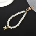 Detailed close-up of an elegant white pearl strap featuring a golden cross pendant and clasp. - Letter X(X)