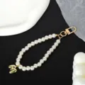 Detail view of a white pearl phone strap with a golden number three pendant ornament. - Letter M(M)