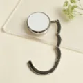 Detailed close-up of a foldable metal handbag hanger hook with a white circular top. - Folding Hook / White
