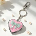 Nahaufnahme eines rosafarbenen Herz-Taschenspiegel-Schlüsselanhängers mit Schleife - Rosa Spiegel Grüne Schleife