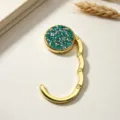 Detailopname van een opvouwbare gouden metalen tassenhaak met groene strassteentjes - Dubbellaagse Strass Opvouwbare Stijl / Smaragdgroen