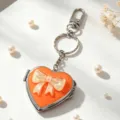 Nahaufnahme eines orangefarbenen Herz-Schlüsselanhängers mit Perlmuttschleife - 橙色镜面黄色蝴蝶结款