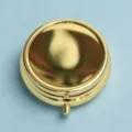 Macro view of a portable golden metal pill box with a secure button latch mechanism. - Gold Round Plain Model