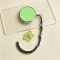 Detail view of a portable foldable metal bag hook with a smooth light green round top - Folding Hook / Green
