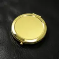 Elegante ronde gouden metalen draagbare zakmake-upspiegel op zwart lederen oppervlak - Verpakking van 1000 / Goud