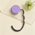 Close-up of a portable purple foldable bag hanger on a clear display plate. - Folding Hook / Purple