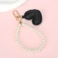 Gedetailleerde weergave van een zwarte hartvormige hanger en witte parellus met goudhaak - Witte Kralenketting + Zwart Hart