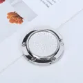 Primer plano de un gancho plegable plateado portátil para bolsos con incrustación texturizada - Estilo de Cuero Sintético Completo / Blanco