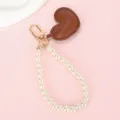 Detailopname van een bruin lederen hartbedeltje met elegante parelketting en goud - Witte Kralenketting + Rood Hart