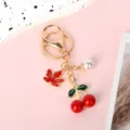 Close-up detail of golden metal keychain featuring red cherry, maple leaf and pearl charms - Maple Leaf Cherry Lobster Buckle