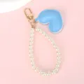 Detail van een blauw kunstleren hartje met een parelmoer bandje en een gouden sluiting. - Witte Kralenketting + Blauw Hart