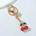 Detailed macro view of vibrant red resin cherry and flower charms on a golden keychain. - Red Cherry Sakura