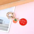 Close-up of a gold-plated keychain with a red lucky charm and persimmon pendant - Circle Everything Goes Well (Persimmon Charm)